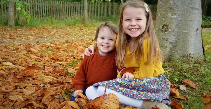 Girl and boy smiling sat in autumn leaves