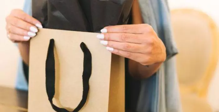 Brown paper shopping paper with black handles held by woman