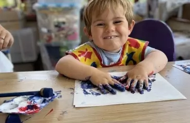 Little boy smiling while doing messy play painting