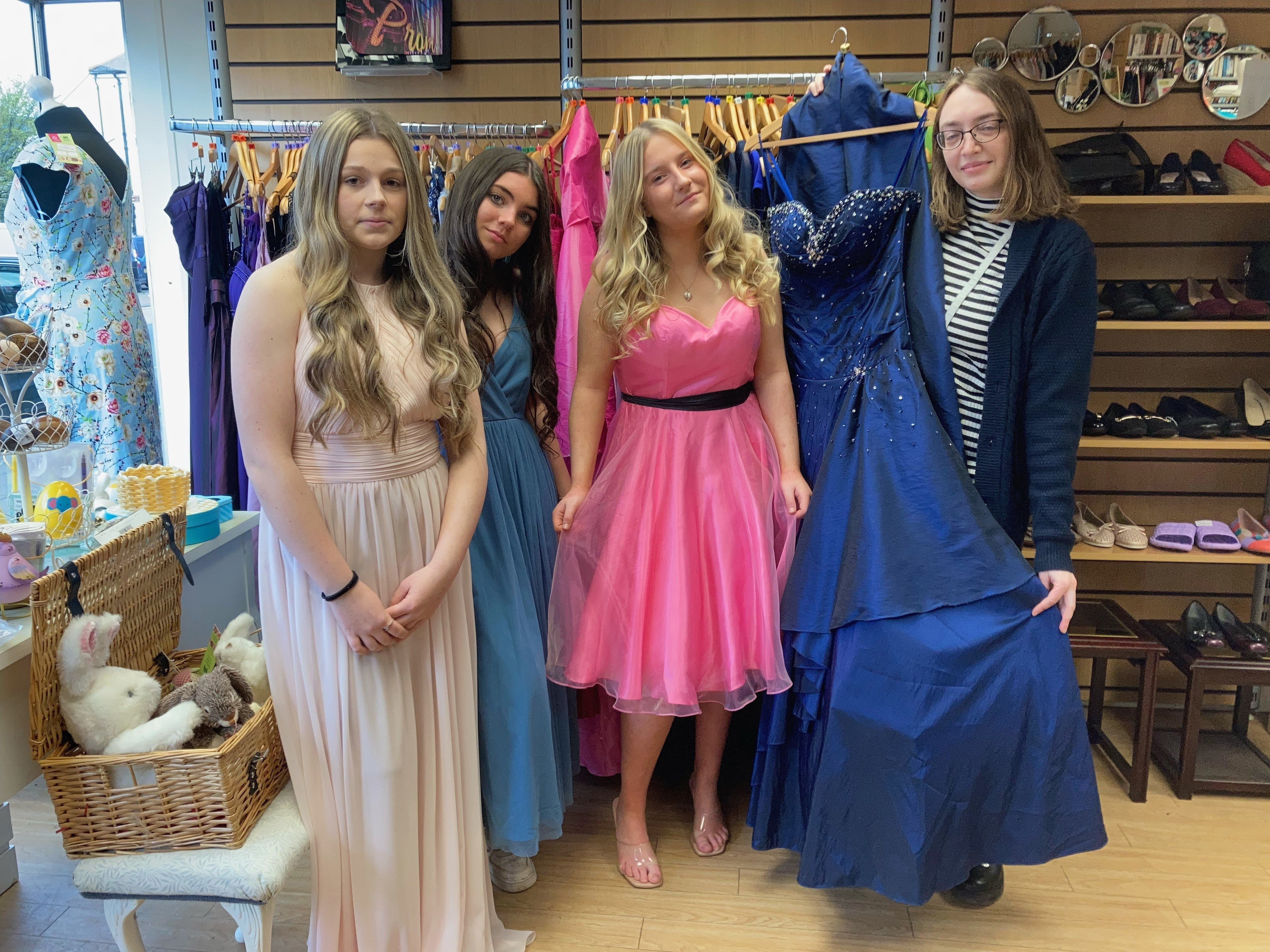 Honiton Community College students Ella-Mae Salter, Lian Galloen and Tia Rush try on some of the dresses with shop volunteer Emma Weir