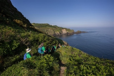 4 hikers walking along the coast path with deep blue sea to the right.