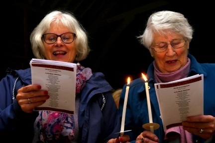 Two ladies singing carols at candlelight