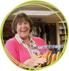 Smiling female volunteer in a shop next to a clothes rack CHSW Volunteer