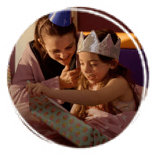 Girl wearing silver crown sat down opening a present