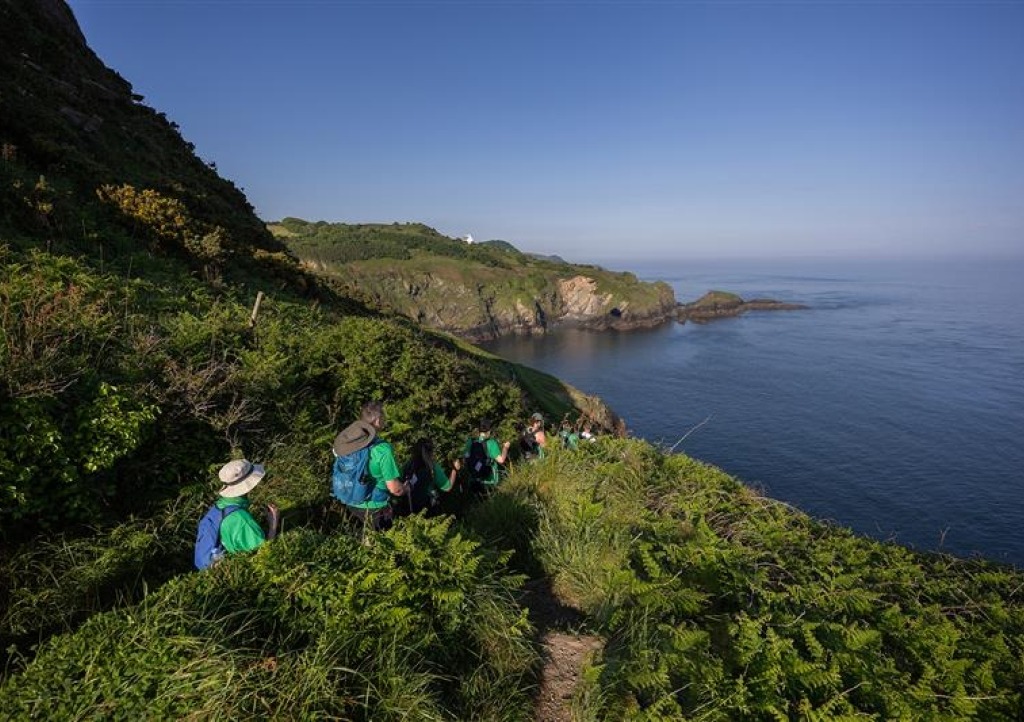 4 hikers walking along the coast path with deep blue sea to the right.