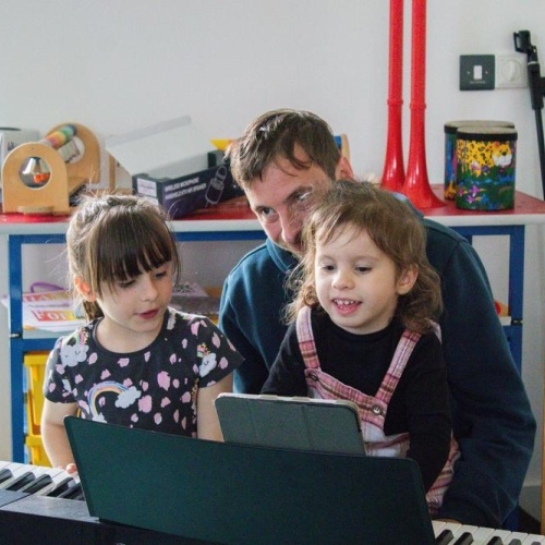 Two sisters and their dad playing the keyboard