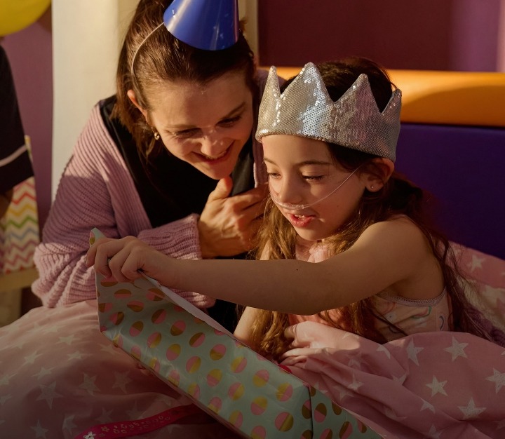 Girl wearing silver crown sat down opening a present