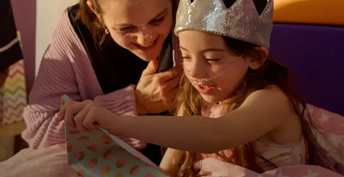 Girl wearing silver crown sat down opening a present