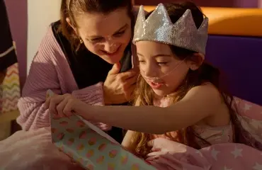Girl wearing silver crown sat down opening a present